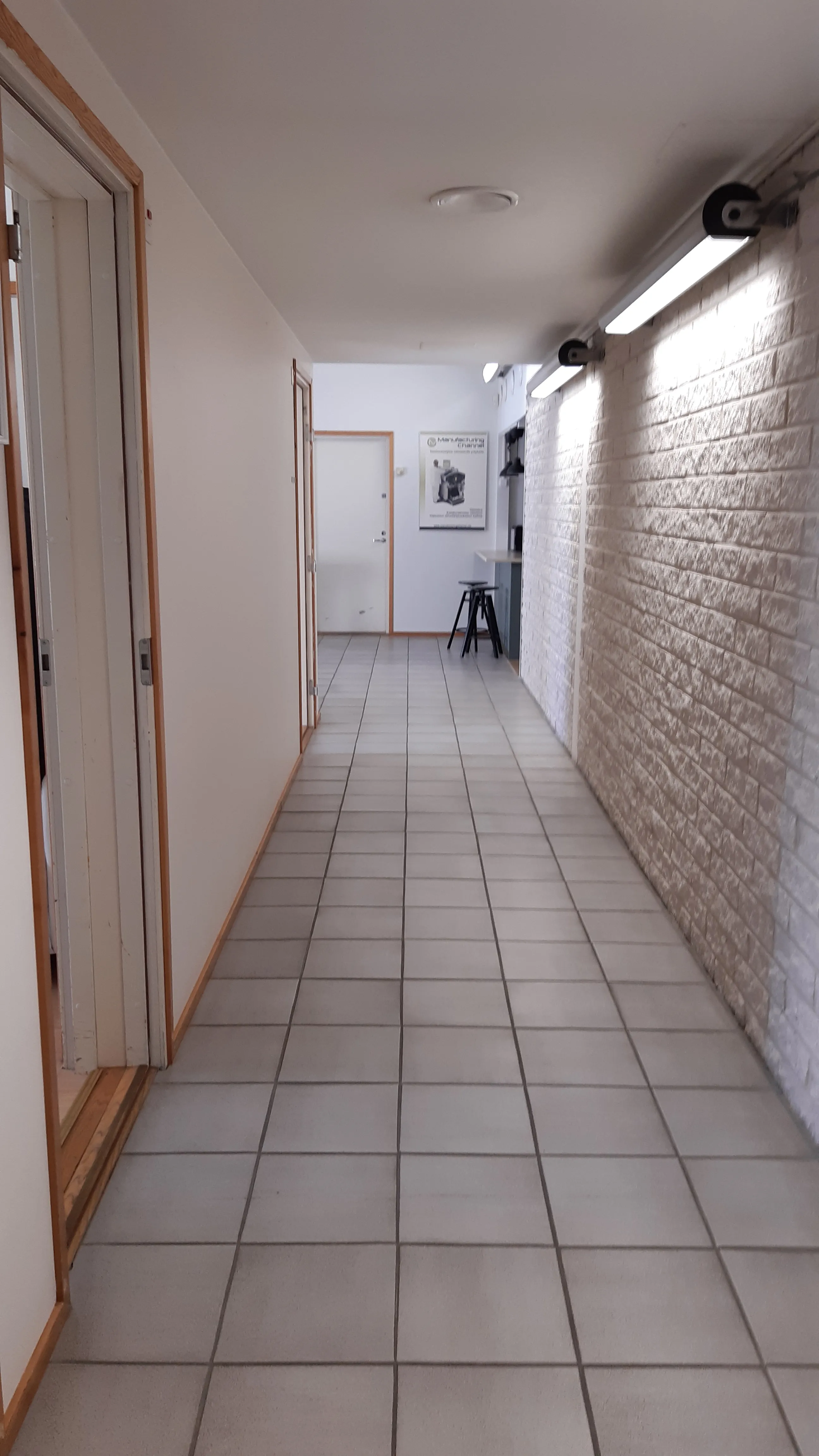 Pitkä käytävä, vaalea tiililaattalattia ja toimistohuoneiden ovet