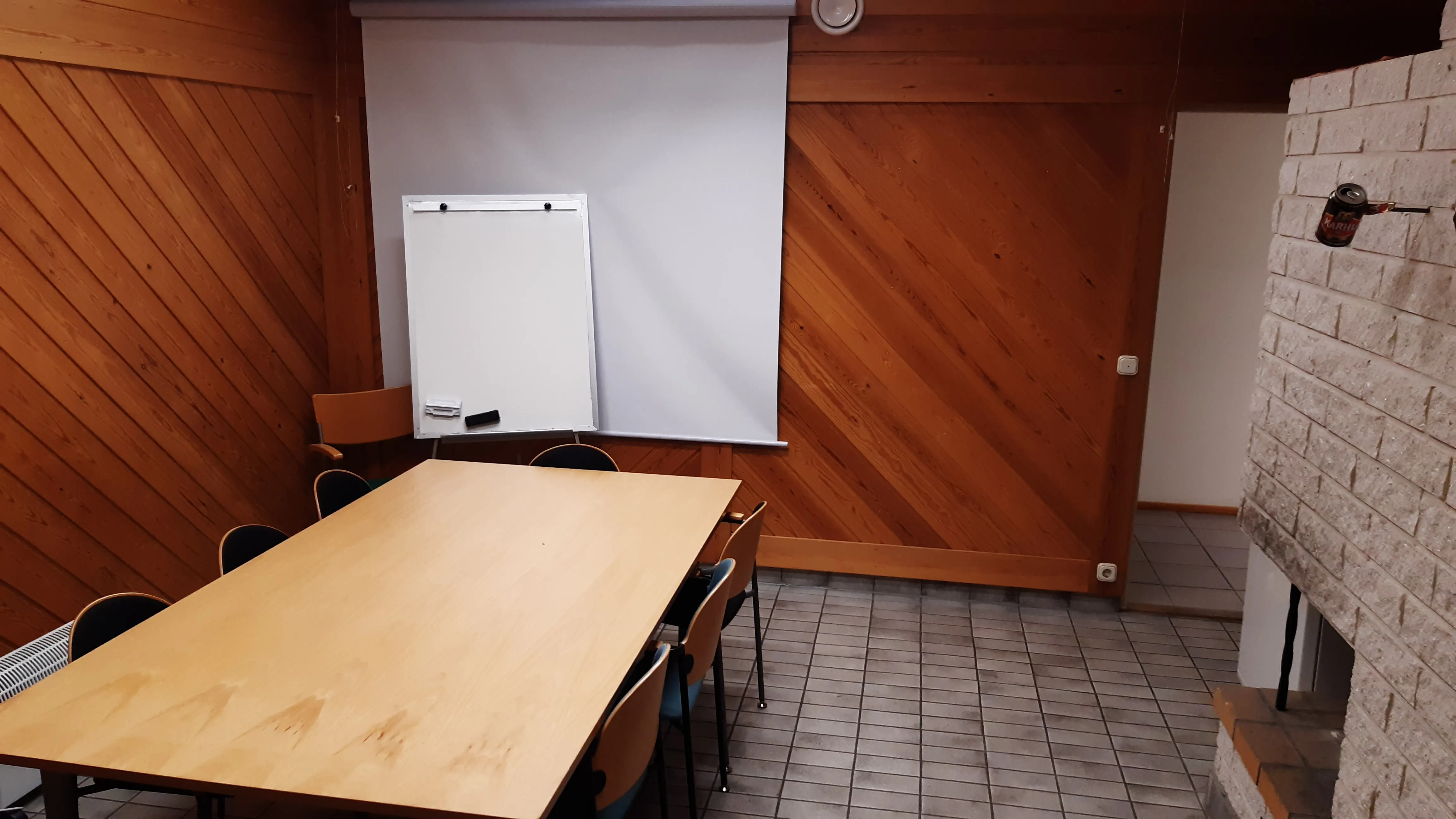 Neuvotteluhuone, jossa on pitkä pöytä, valkokangas ja puuseinä