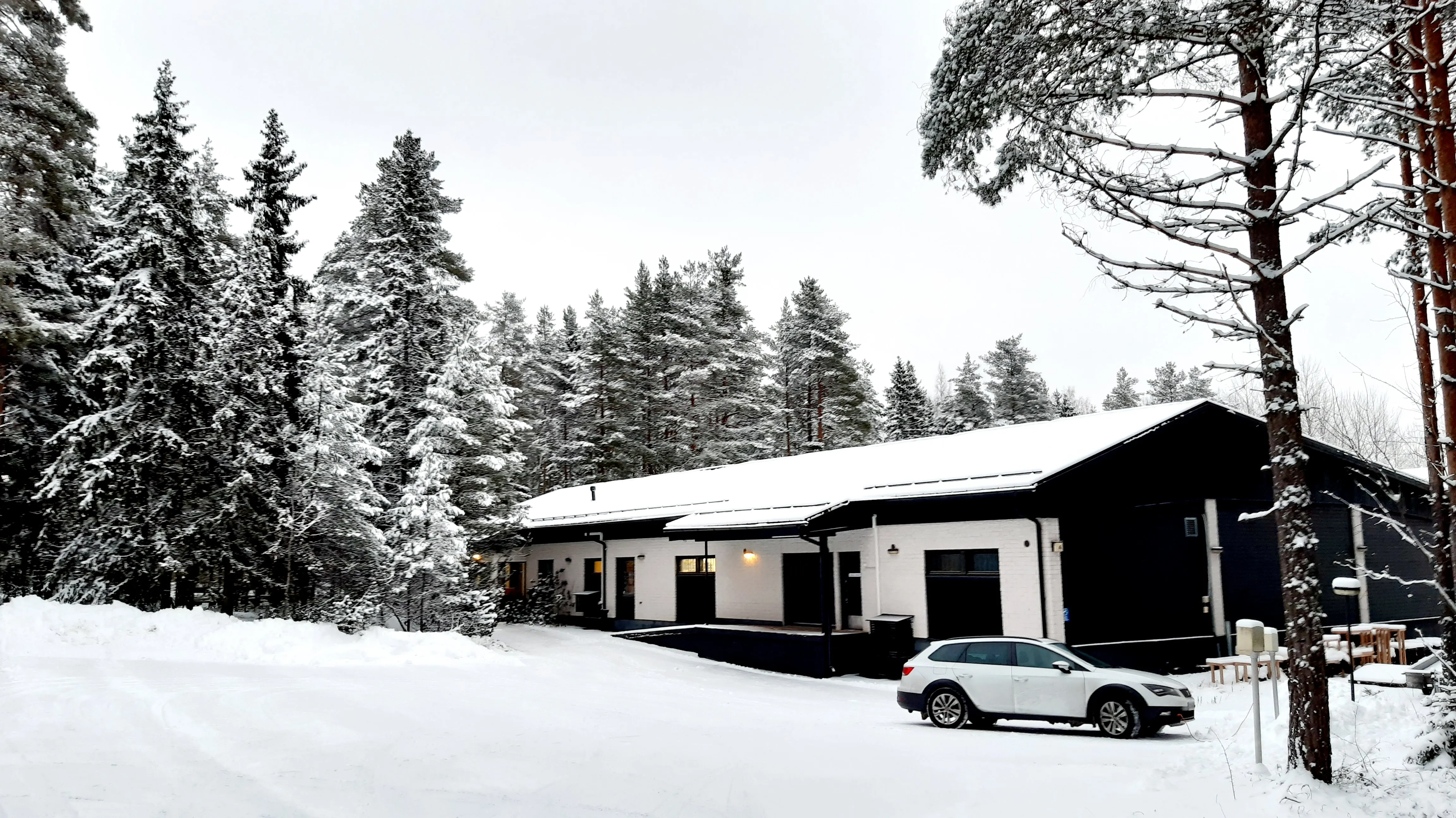 Toimistorakennus lumisen metsän reunassa, auto pihassa